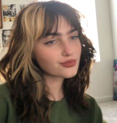 a close up of a person wearing a green shirt and long wavy hair with bangs