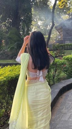 a woman in a yellow sari is looking at the trees and bushes behind her