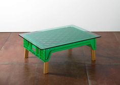 a green table sitting on top of a brown floor next to a white wall in an empty room