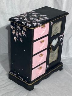 a black and pink dresser with flowers painted on the front, drawers are decorated with hearts