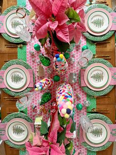 the table is set with pink flowers and green placemats, plates and napkins