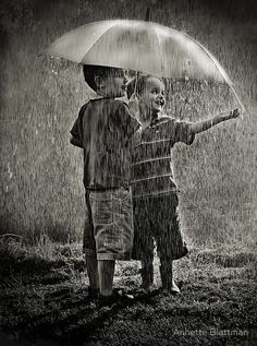 two children standing in the rain with an umbrella