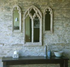 two mirrors on the wall above a table with a bowl and vase next to it