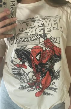 a person holding a cell phone and wearing a spiderman t - shirt