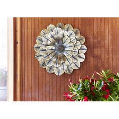 a wall hanging on the side of a wooden door next to potted plants and flowers