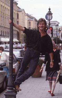 a man standing on top of a street light pole next to a woman walking down the sidewalk