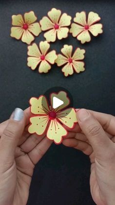 two hands are holding some paper flowers on a black surface with red and yellow petals