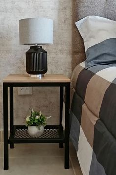 a nightstand with a lamp on top of it next to a plaid bed spread and pillow