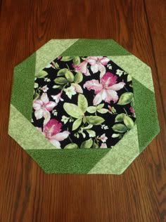 a black and green patchwork table topper with pink flowers on it sitting on a wooden surface