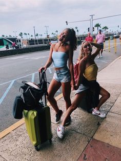 two young women sitting on the curb with their suitcases and bags in front of them