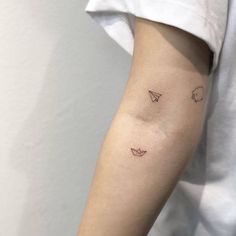 a woman's arm with small tattoos on the left side of her arm and an origami paper airplane in the middle