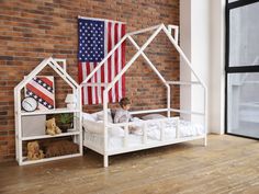 a little boy sitting in his bed with the american flag hanging on the wall behind him