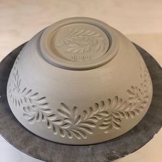 a white ceramic bowl on top of a black plate with a silver base and leaf decoration