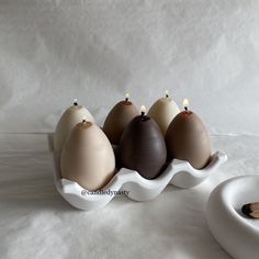 five different colored eggs in a white egg shell on a table with a bowl and spoon