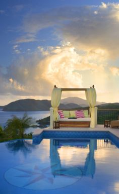 an outdoor pool with a gazebo and lounge chairs overlooking the ocean at sunset or sunrise