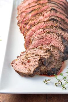 a piece of steak on a white plate with garnish and sprigs