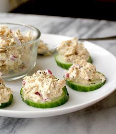 small cucumbers filled with chicken salad sit on a plate next to a glass bowl