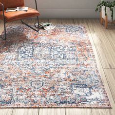 an orange and blue area rug with a chair in the corner, next to a potted plant