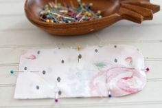 a wooden bowl filled with pins and needles next to a piece of fabric on a table