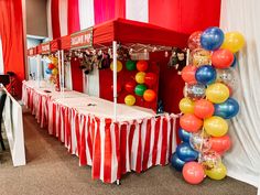 a red and white striped tent with balloons on the table in front of it at an event