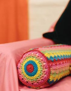 a crocheted blanket laying on top of a bed next to a black pillow