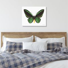 a green butterfly sitting on top of a bed in a white room with plaid sheets and pillows