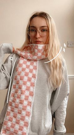 a woman wearing glasses and a knitted scarf is standing in front of a wall