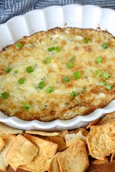 a casserole dish with green onions and tortilla chips on the side