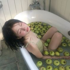 a woman laying in a bathtub filled with green apples