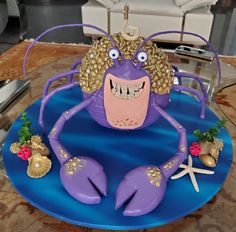 a purple cake decorated with an octopus and starfish on a blue plate in the middle of a room