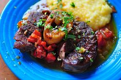 a blue plate topped with meat, potatoes and veggies on top of a wooden table