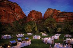 an outdoor dining area with tables and chairs set up in front of red mountains at dusk