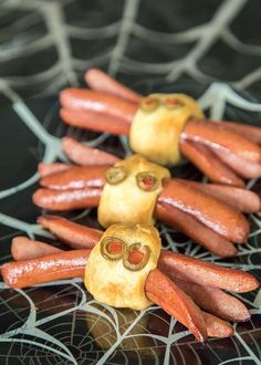 some hot dogs with googly eyes are on a black plate and there is spider web in the background