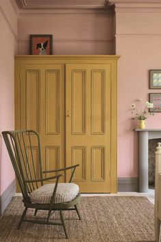 a yellow armoire sitting next to a white chair in a room with pink walls