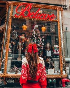 a woman standing in front of a store window with christmas decorations and lights on it