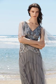 a woman standing on top of a beach next to the ocean wearing a gray dress