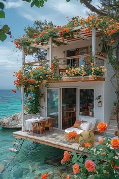 a house with flowers growing on the roof and balcony over looking the ocean in front of it