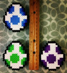 three pieces of perler bead art sitting next to a ruler