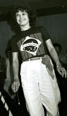 an old photo of a woman in white pants and a black t - shirt smiling