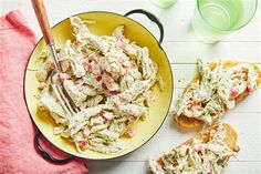 a bowl full of chicken salad next to two slices of bread on a white table