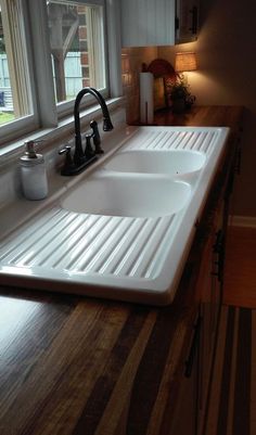 a kitchen sink sitting under a window next to a wooden counter top with two faucets