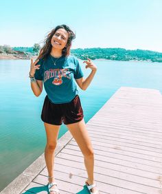 a woman standing on top of a wooden pier next to the water with her hand up