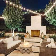 an outdoor patio with wicker furniture and string lights strung over the fire place at night