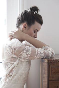 a woman in a white dress is leaning on a table with her arm over her shoulder