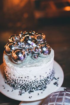 a white cake topped with lots of shiny balls on top of a wooden table next to a cookie