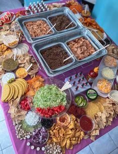 a table topped with lots of food on top of a purple table cloth covered in condiments