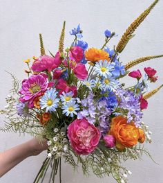 a person holding a bouquet of flowers in front of a white wall with blue, pink and orange flowers