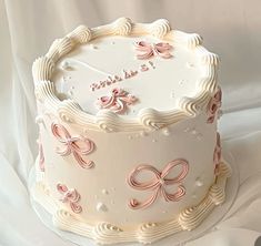 a white cake decorated with pink bows and writing on the top is sitting on a table