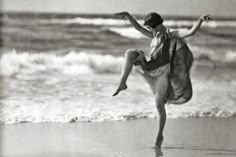 a black and white photo of a woman dancing on the beach