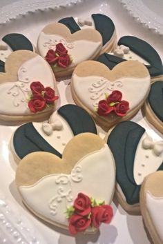 decorated cookies in the shape of hearts on a white platter with red roses and blue ribbon